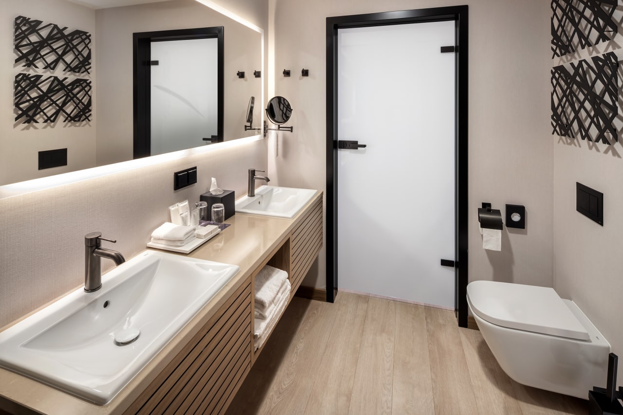 The interior design by Tremend Studio features a cohesive design characterised by the use of warm, natural tones and wood elements that create a welcoming and serene atmosphere. The guest bathrooms feature walk-in showers with glass enclosure creating a spacious and open feel or cosy drop-in bathtubs. A wood-accented vanity with a Diverta countertop basin and The Gap wall-hung Rimless toilet maintain the luxurious yet homely ambiance. The public restrooms continue the theme of modern minimalism with its clean and uncluttered layout, featuring Diverta basins and Hall urinals. The use of integrated LED lighting behind enhances the mirrors enhances the space with a soft glow, providing ample illumination while adding a touch of sophistication.2